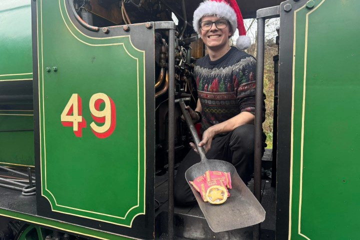 Person in Santa hat on green train with the number 49, holding a shovel with coal.