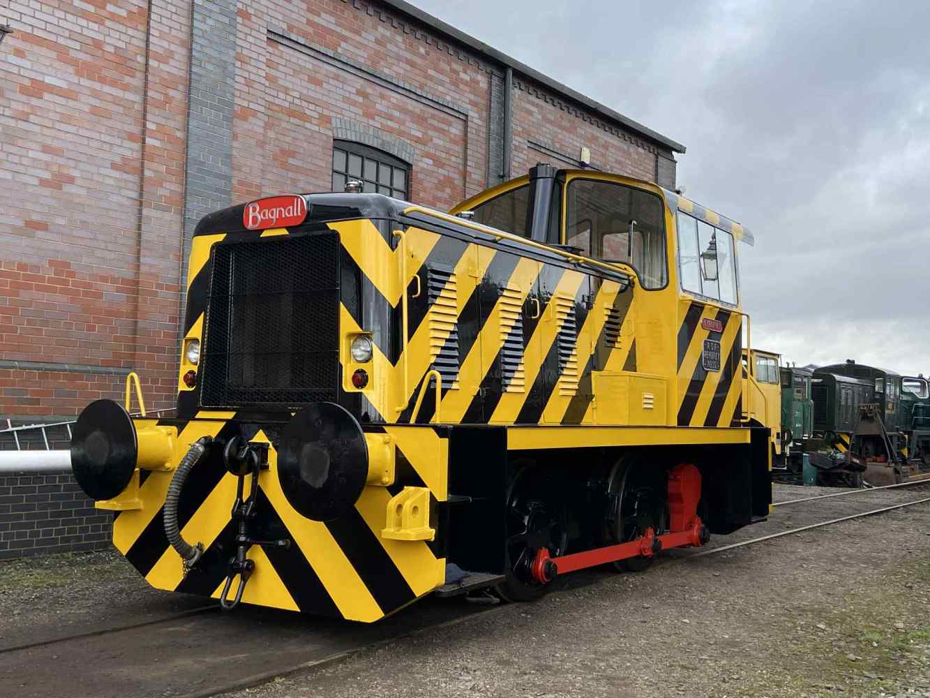 Yellow and black striped train engine outside a brick building on a cloudy day.