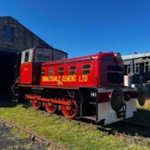 Red vintage train engine beside a shed with a blue sky background.