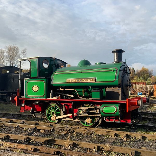 Green vintage steam locomotive on railway tracks under cloudy sky.