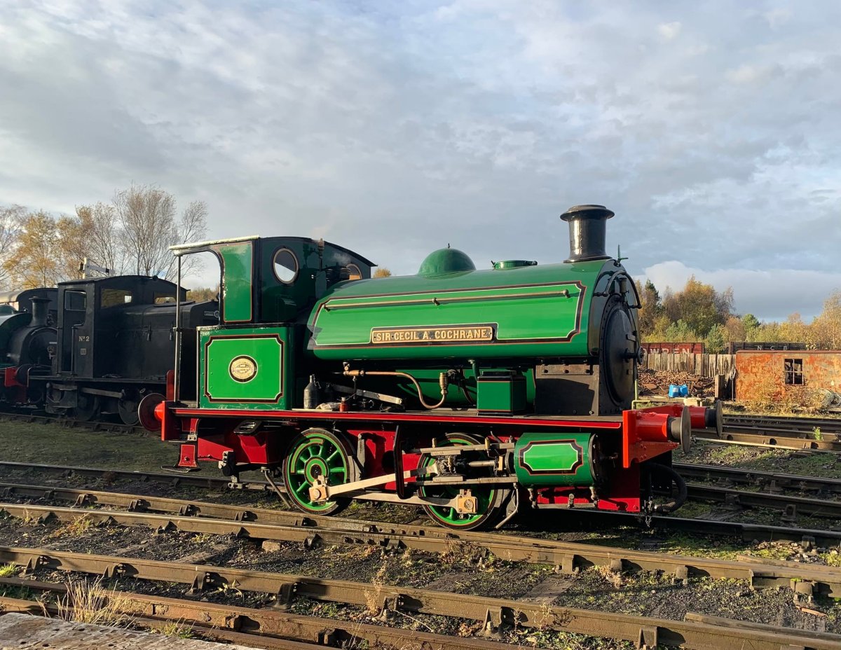 Sir Cecil A Cochrane Green vintage steam locomotive on railway tracks under cloudy sky.