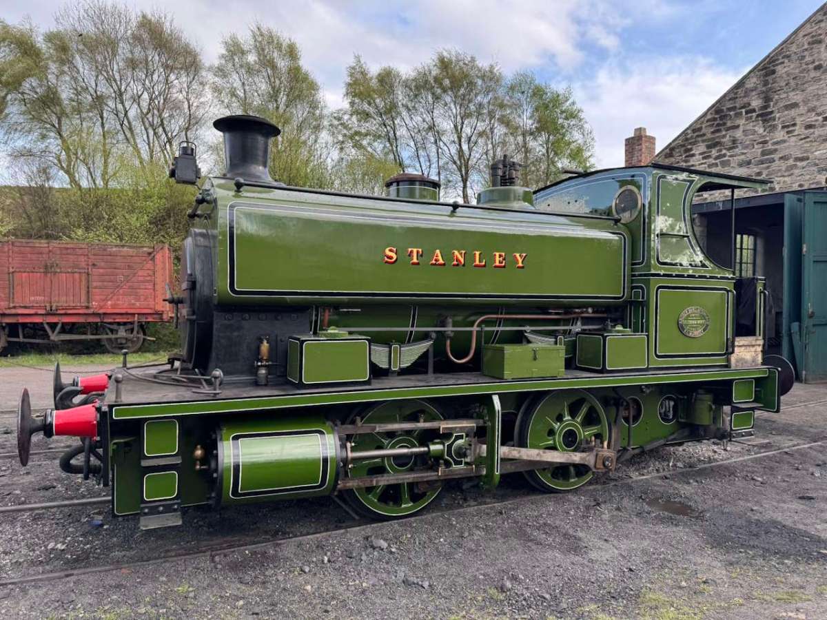 Stanley-steam-engine-at-Tanfield-Railway Green steam locomotive named 'STANLEY' parked outdoors near trees and a shed.