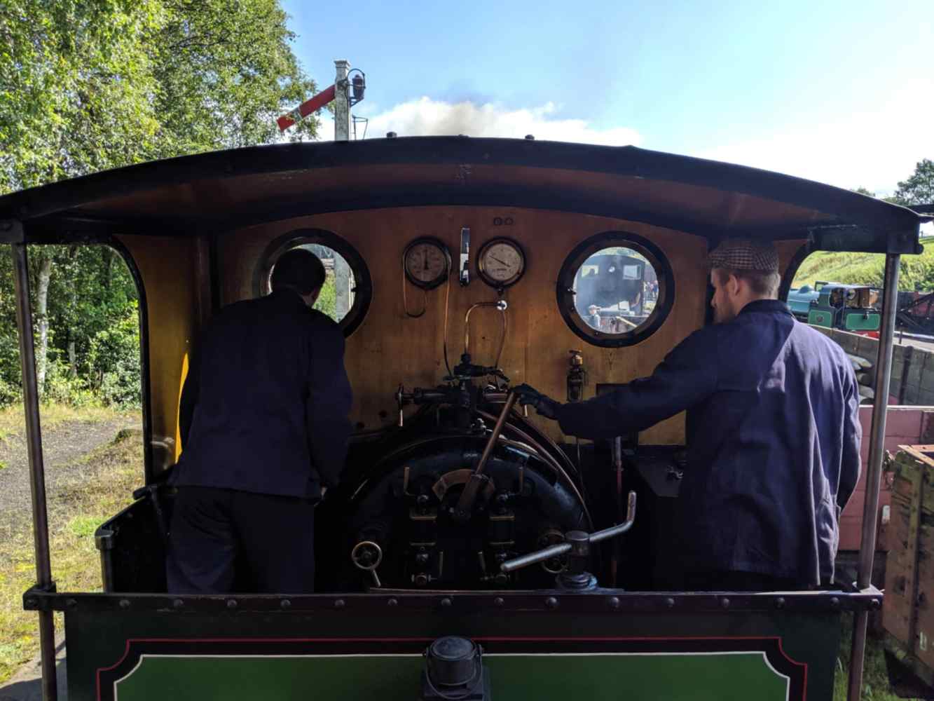 Two people operating a vintage steam locomotive on a sunny day.
