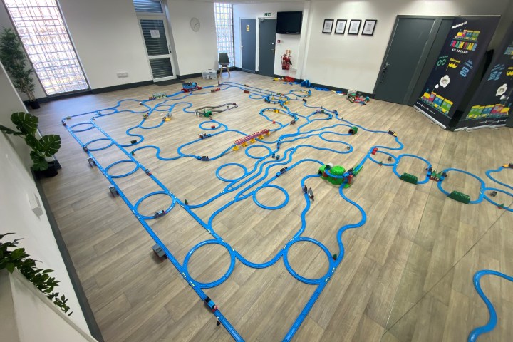 Large toy train track layout on a wooden floor in a well-lit room.